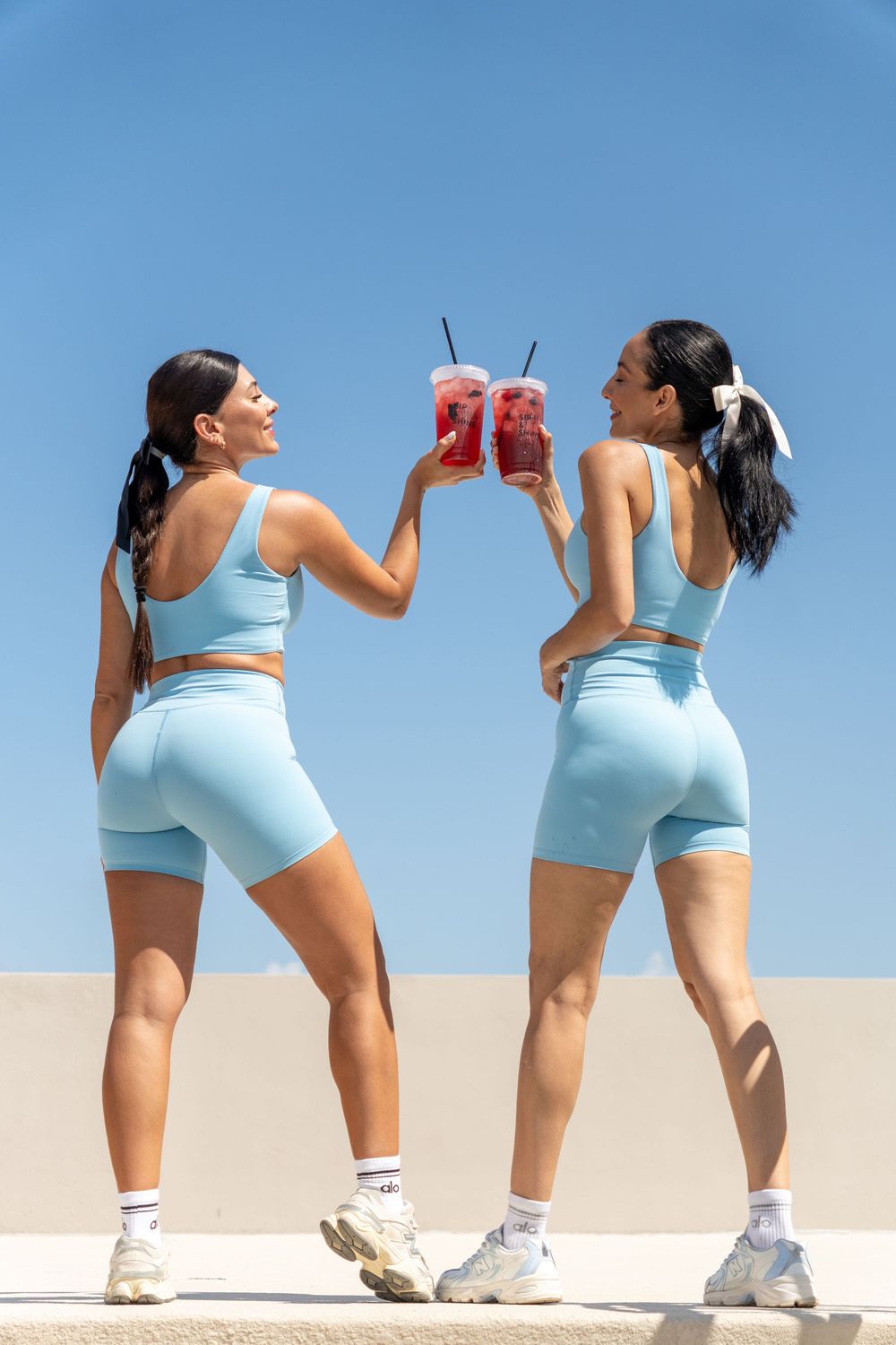 Two fitness creators celebrating with branded Sip & Shine drinks under a clear blue sky, showcasing an active lifestyle.