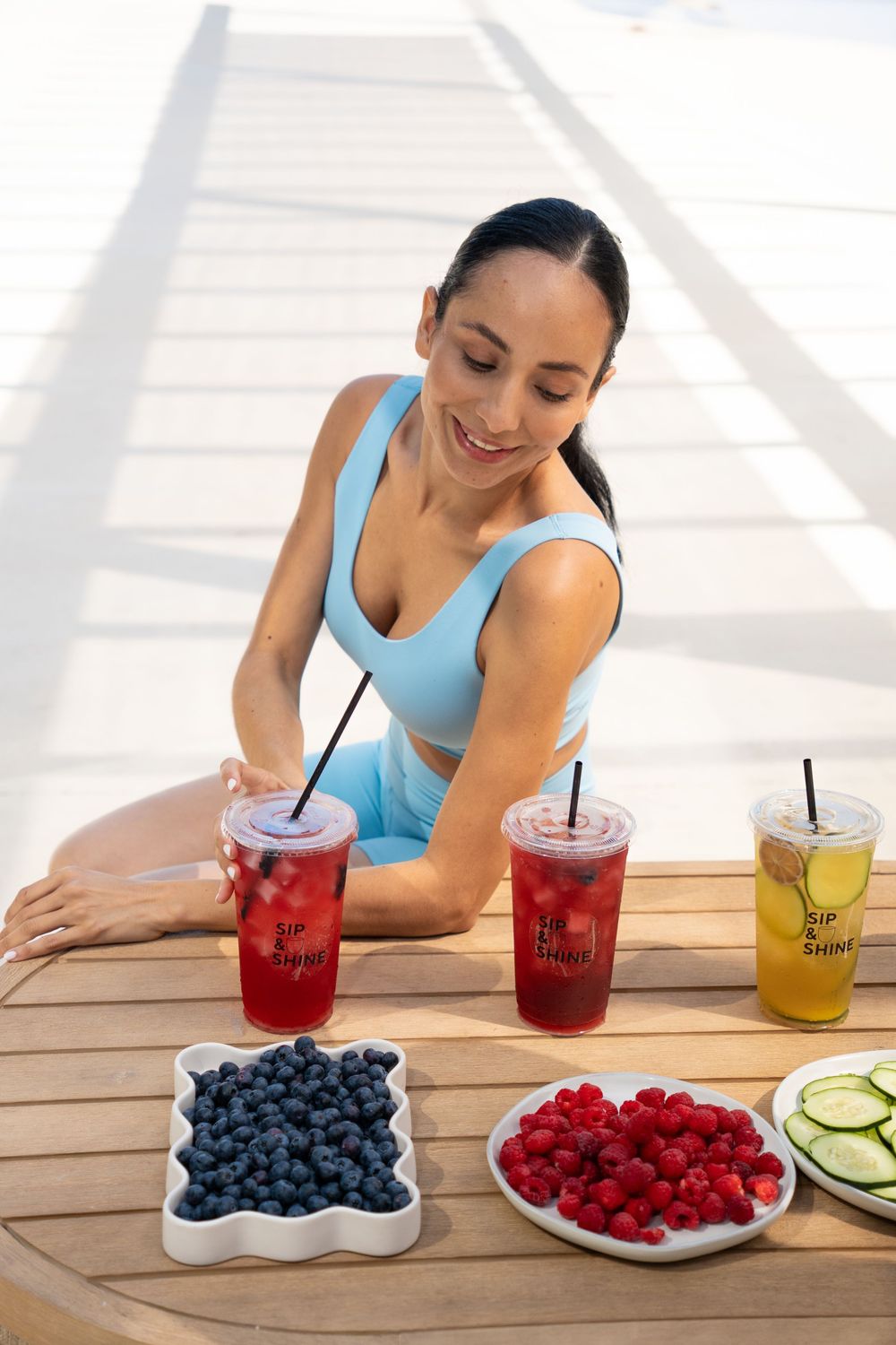 Fitness model enjoying colorful Sip & Shine drinks with fresh fruit, showcasing healthy ingredients and wellness lifestyle.
