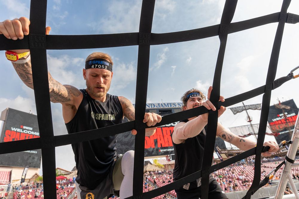 Athlete climbing a Spartan cargo net obstacle from a dynamic low angle, emphasizing focus, agility, and determination.