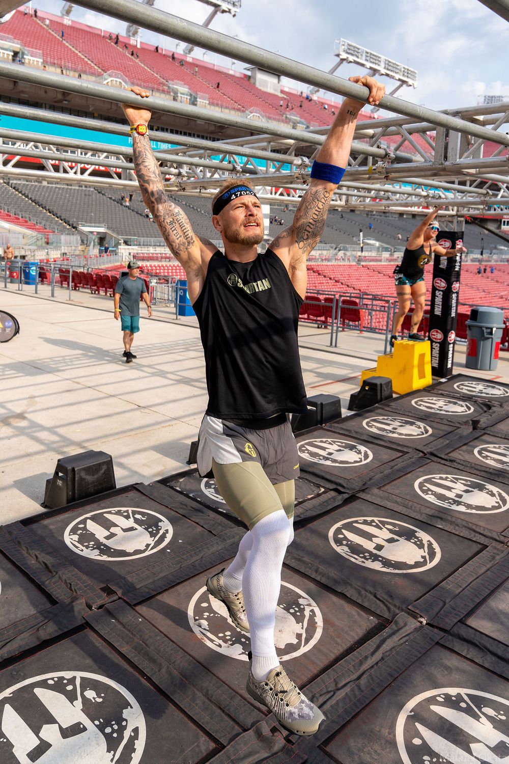 Athlete crossing Spartan monkey bars obstacle during stadium race, highlighting grip strength, endurance, and determination.