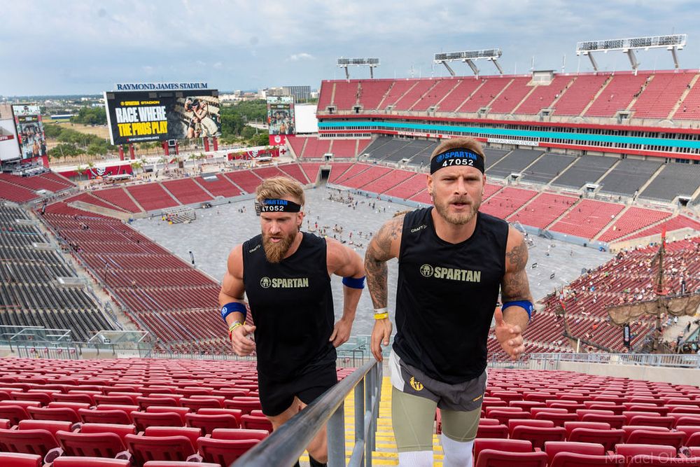 Two Spartan athletes sprinting up stadium stairs during training, highlighting teamwork, endurance, and athletic performance.