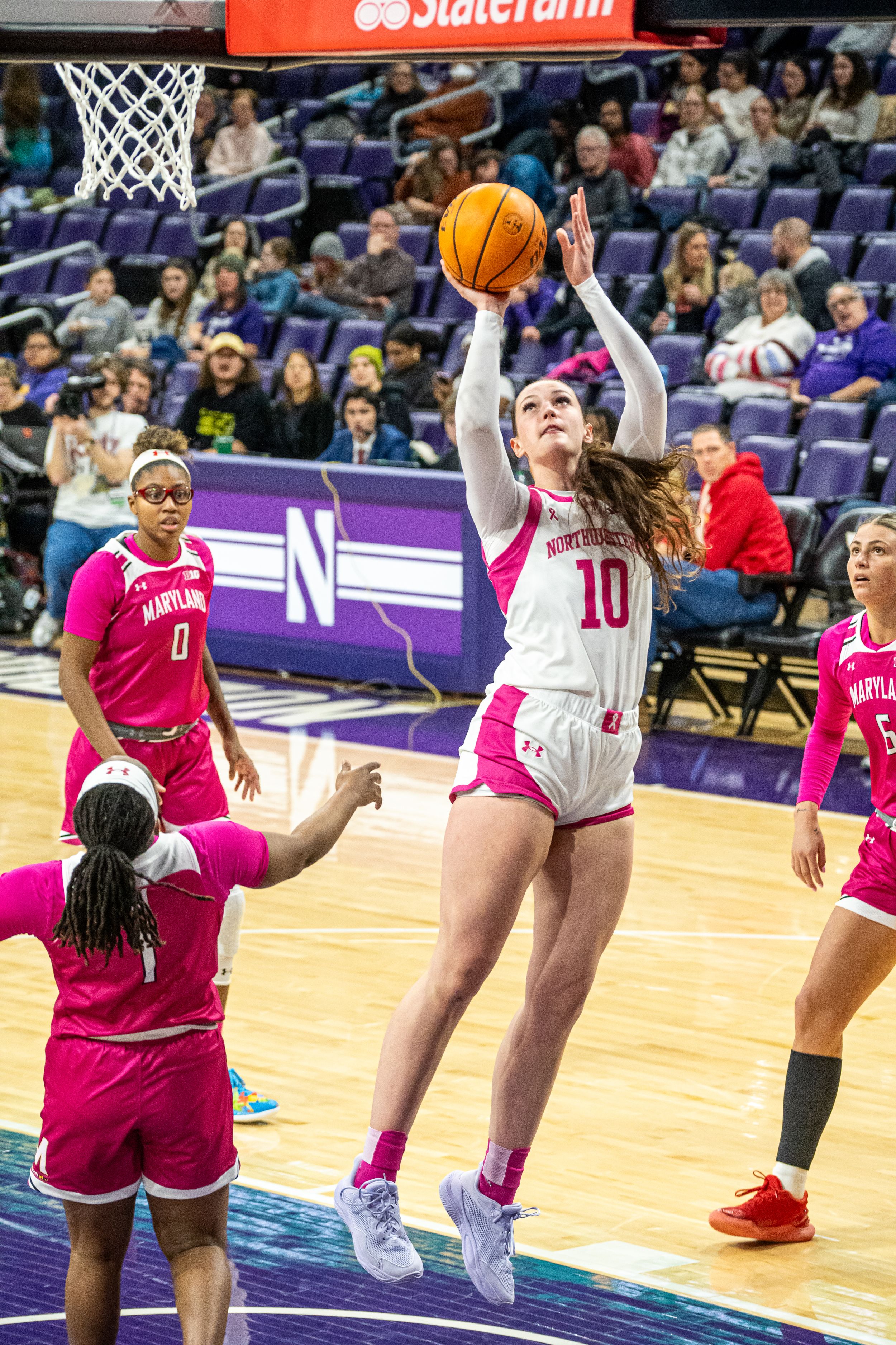 Basketball player in white jersey leaps for a shot over defender in pink uniform during college game at Northwestern.