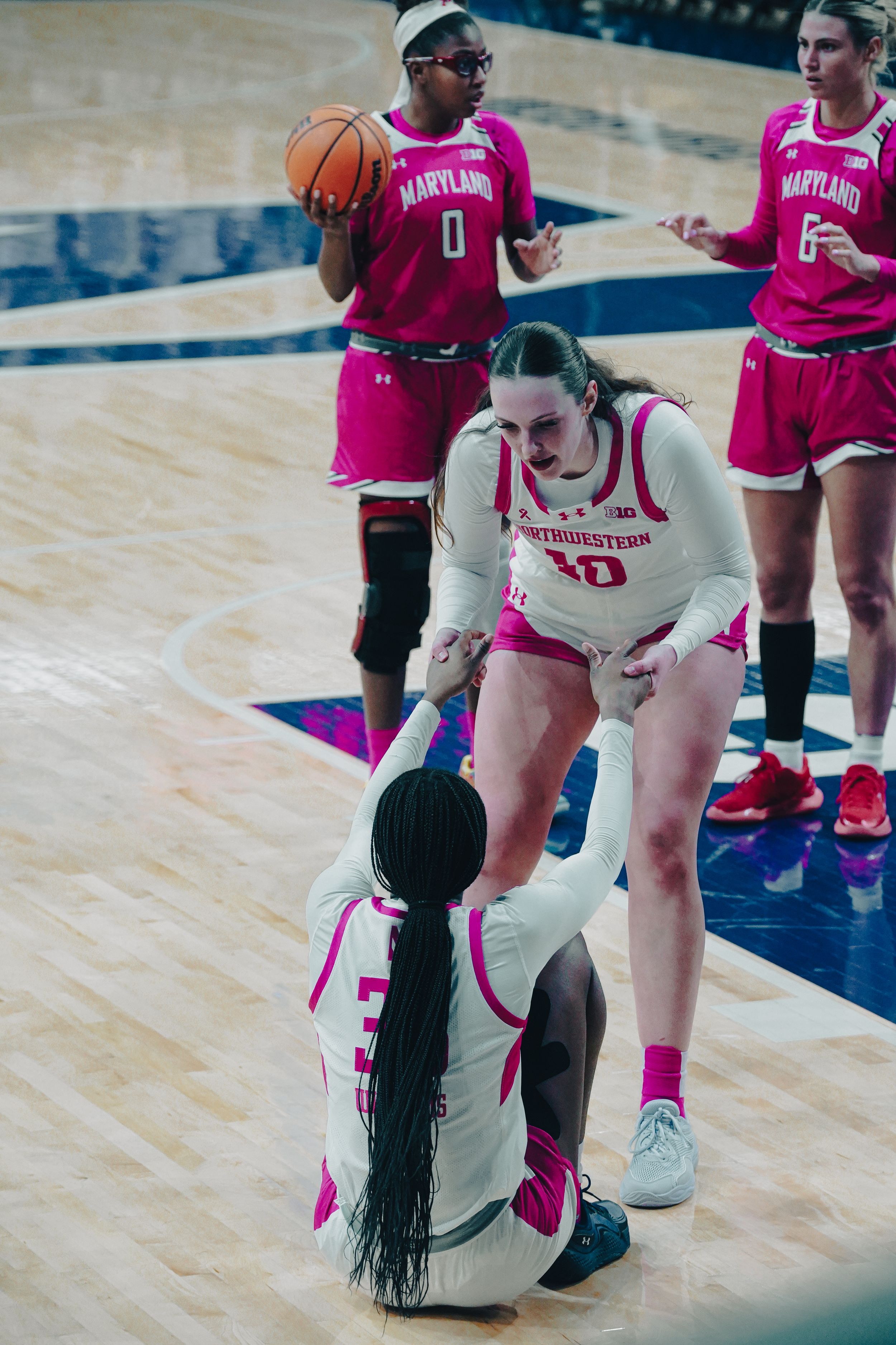 Basketball players in pink Maryland jerseys and white uniforms interact during a competitive game on the court.