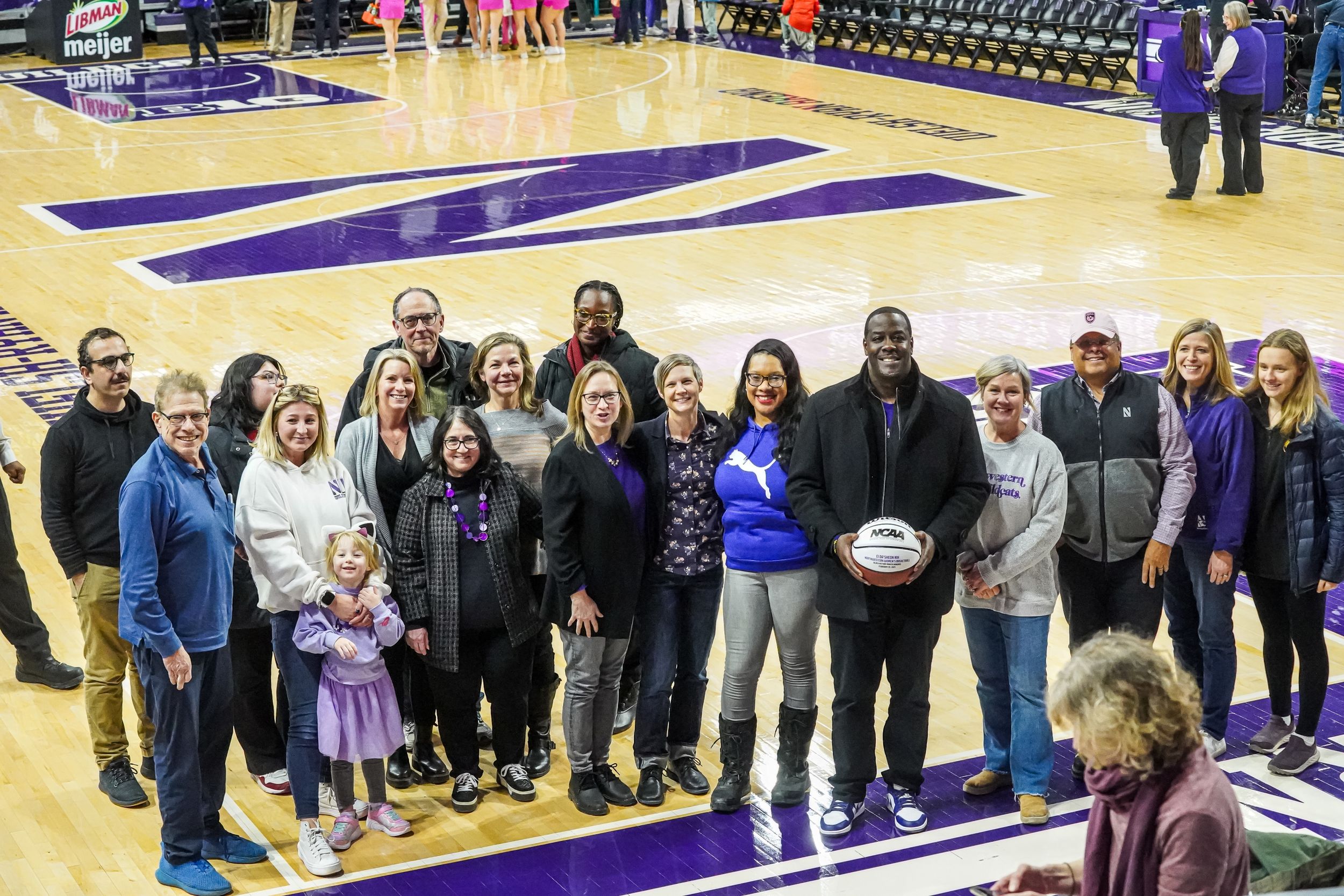 Group photo of people gathered on a basketball court with purple markings celebrating during a sports recognition event.