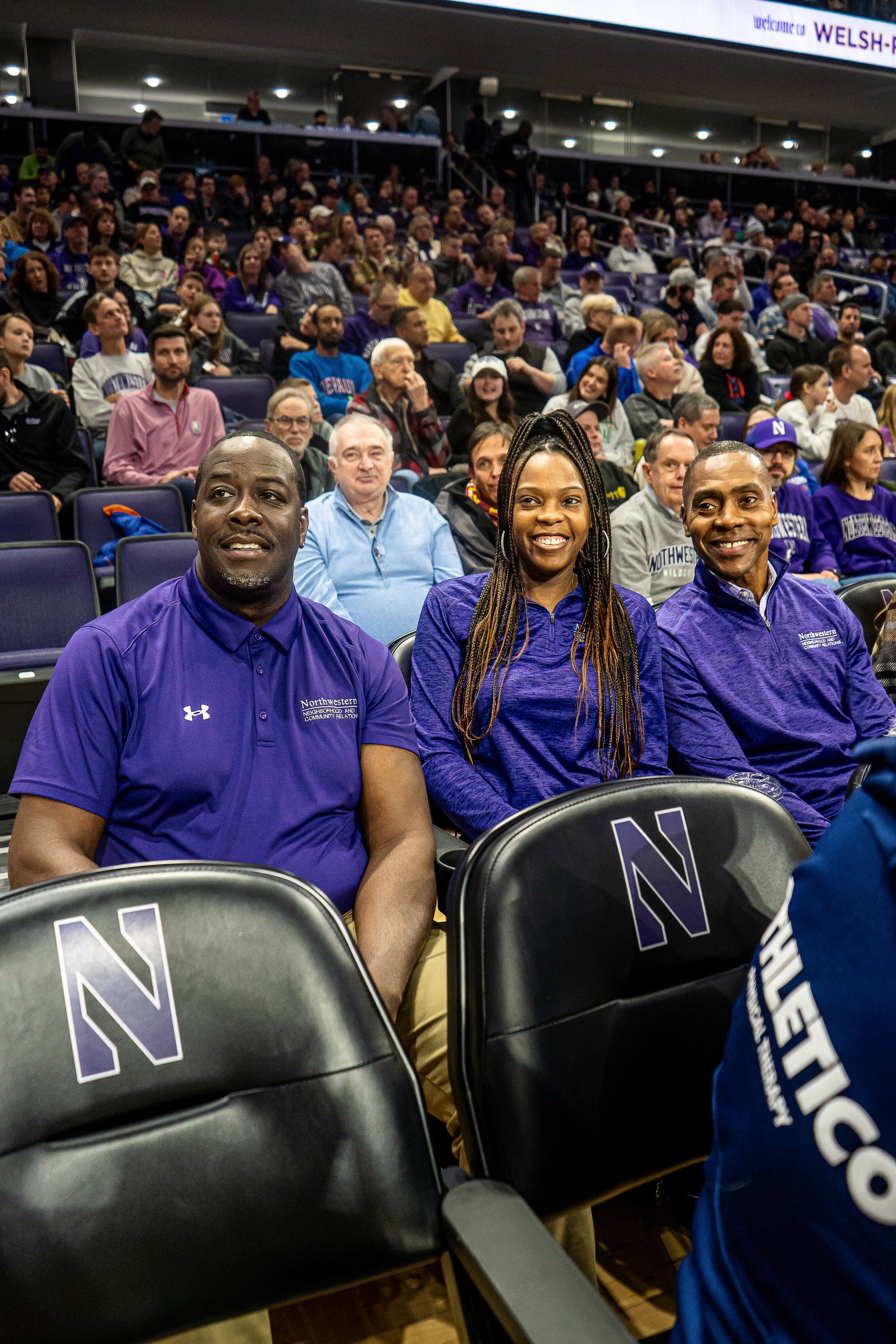 Enthusiastic staff members in purple Northwestern gear sit together in stadium seats at a sporting event.