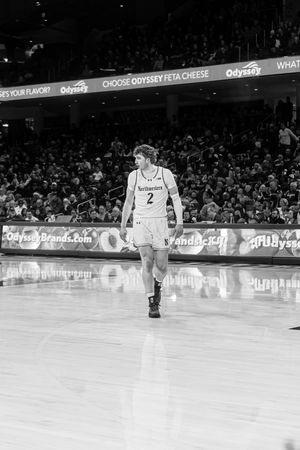 Basketball player in white jersey number 2 walks on court during professional game in black and white photography.