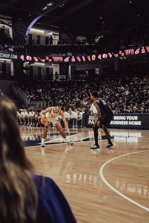 Basketball players face off on court during professional game with crowd and stadium banners in background.