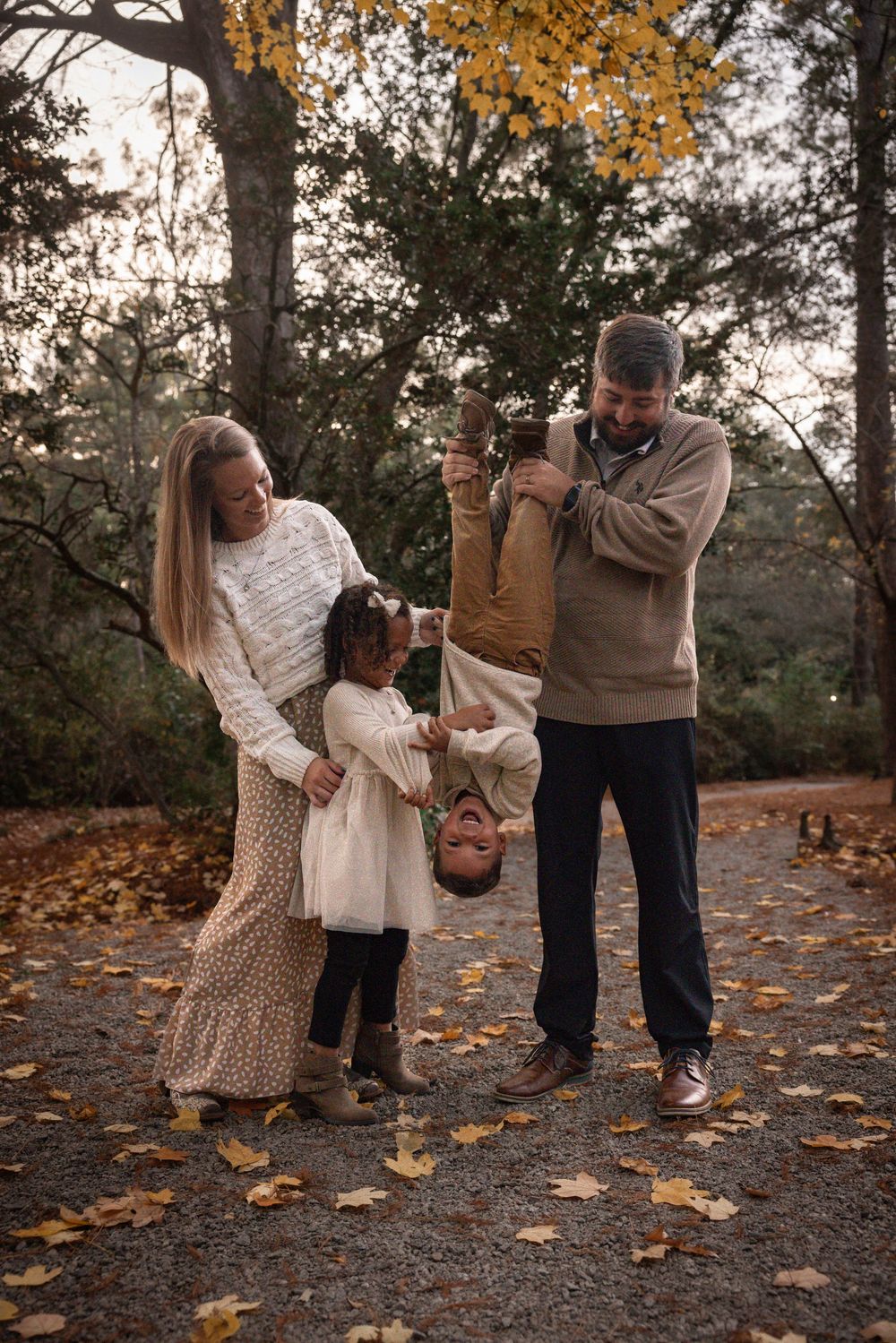 A family plays together in a park during autumn with fallen leaves scattered on the ground.