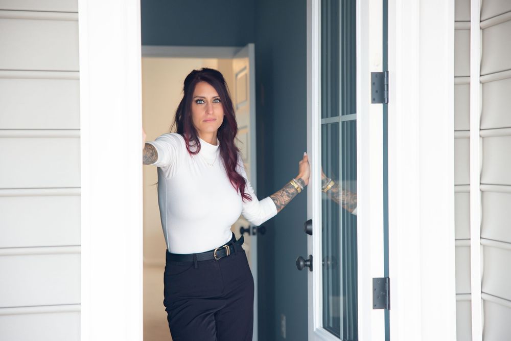 A person in business attire stands in a doorway of a white building with green trim.