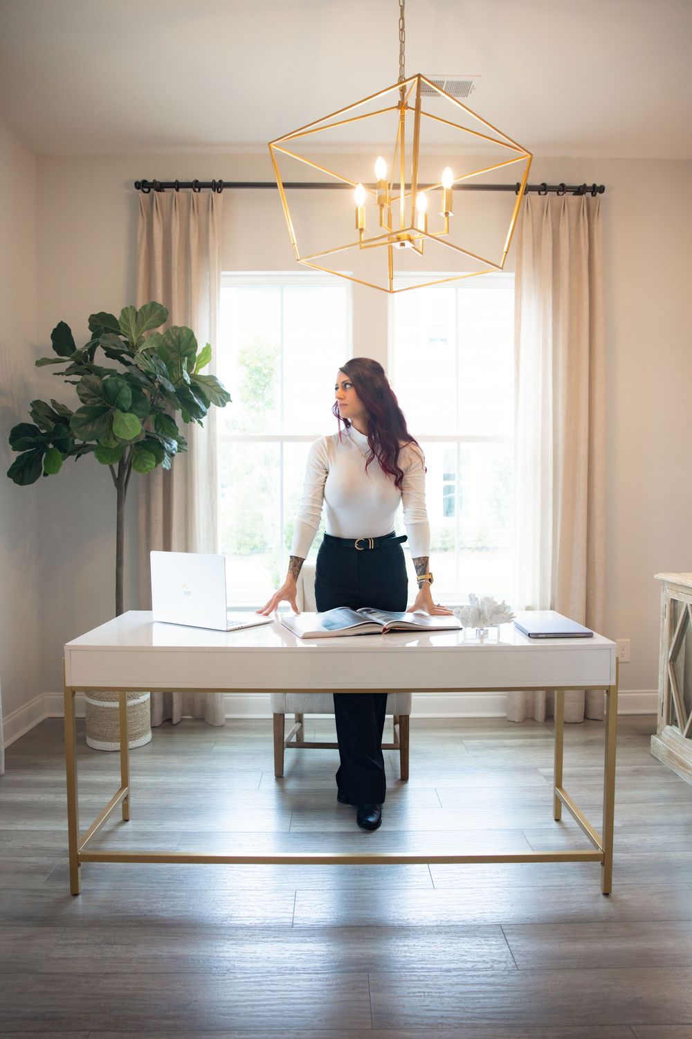 Modern dining room features white walls, wood floors, gold chandelier, and large windows with flowing curtains.