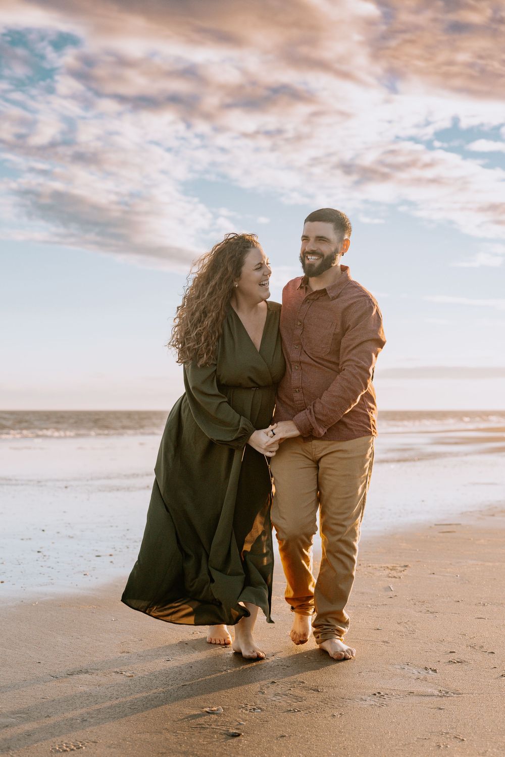A couple shares a romantic moment on the beach at sunset, walking and embracing in the golden light.