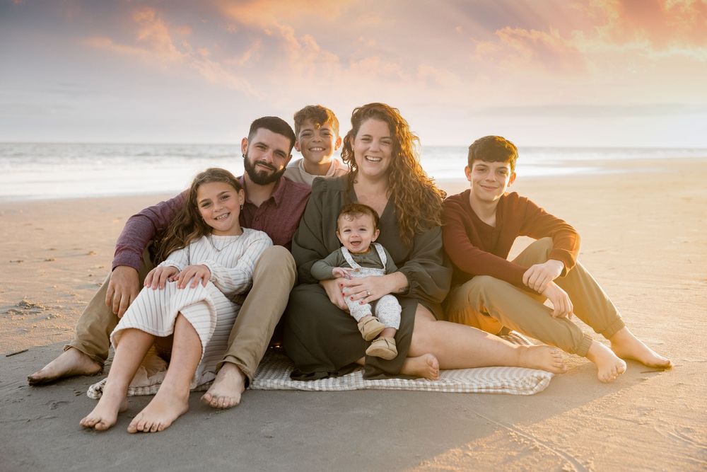 A group relaxes together on a sandy beach during golden hour as the sun sets over the ocean.