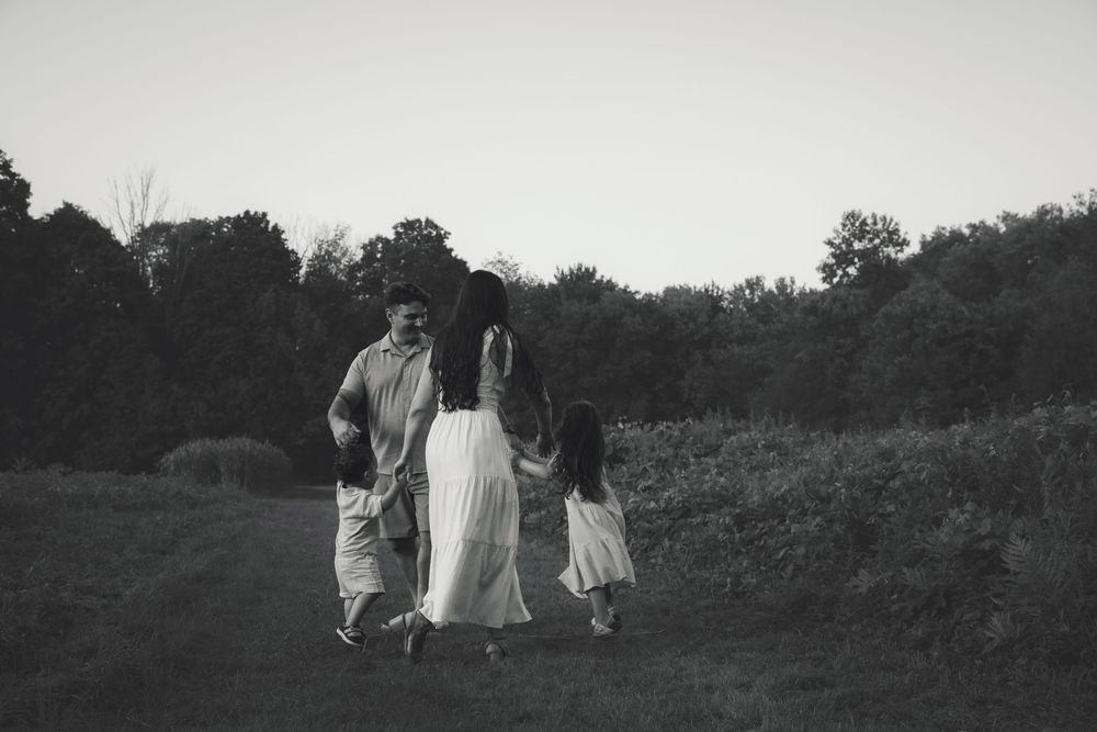 Black and white photo of a family of three walking together in a grassy field with trees in the background.