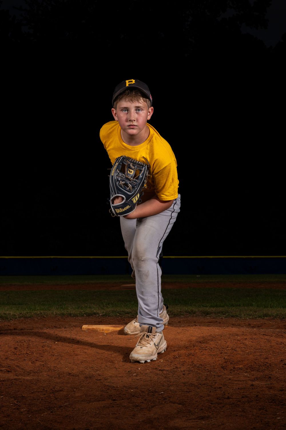 Baseball player in yellow jersey and gray pants pitches from the mound at night under stadium lights.