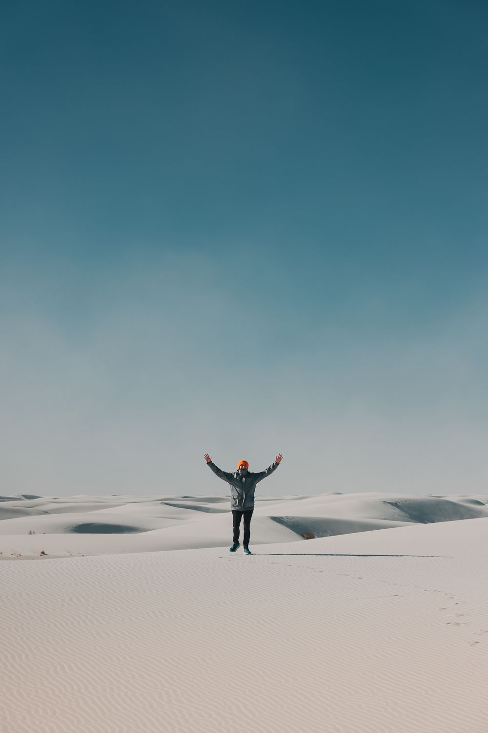 A person stands with arms raised in White Sands National Park, surrounded by vast white gypsum dunes under a clear blue sky.