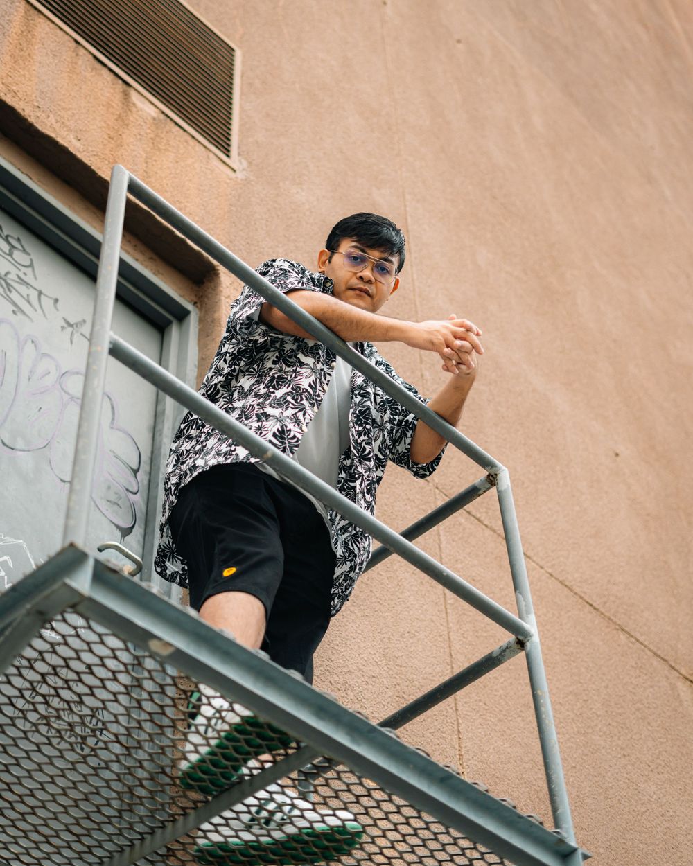 Low angle shot of someone posing on a metal fire escape wearing a floral pattern shirt.
