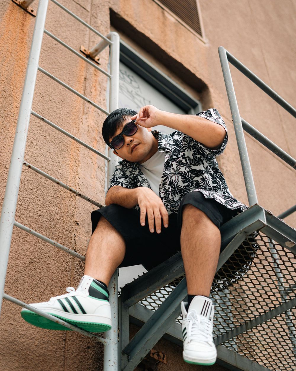 Street style portrait on metal stairs wearing sneakers and a patterned shirt.