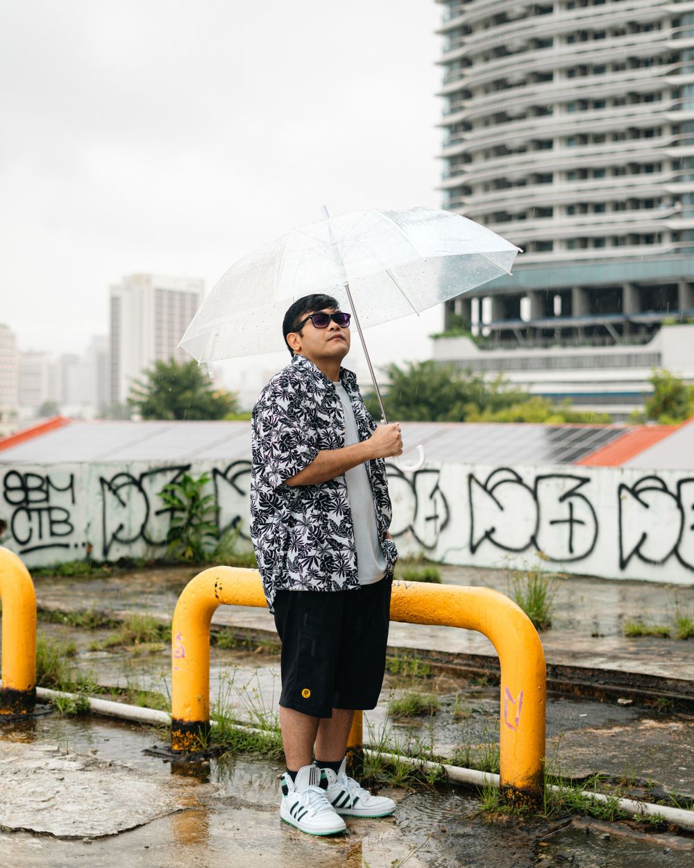 Urban fashion shot with yellow barriers and graffiti featuring a clear umbrella.