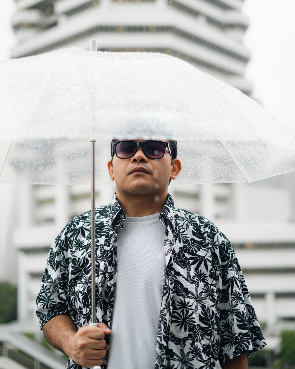 Moody portrait under a clear umbrella with architectural elements in soft focus.