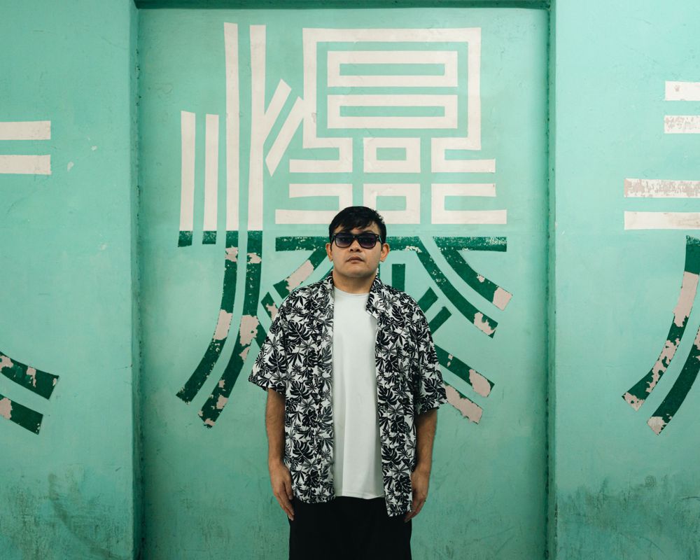 Fashion portrait against turquoise wall with geometric patterns wearing floral shirt and sunglasses.