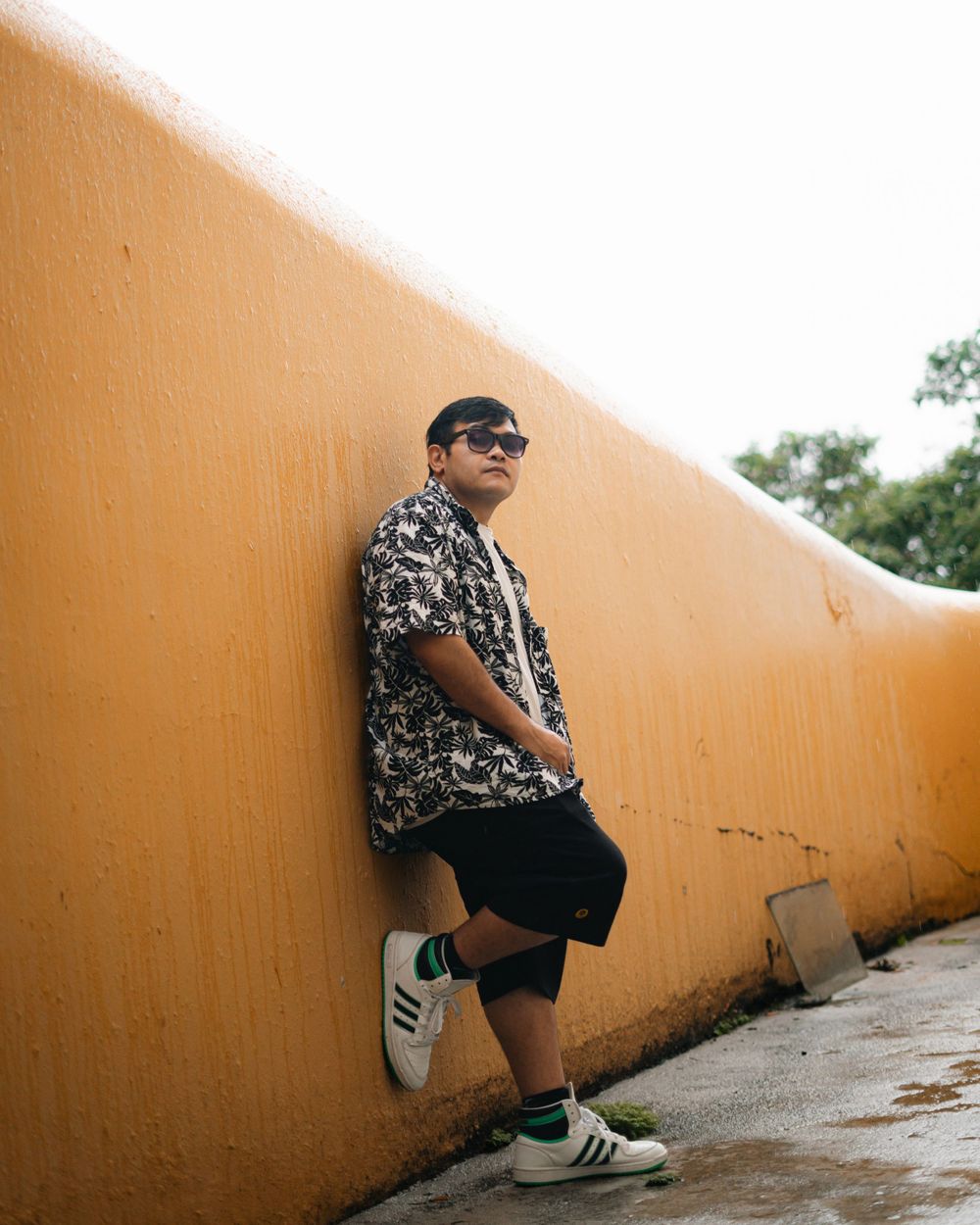 Street style fashion shot against orange wall wearing patterned shirt and shorts.