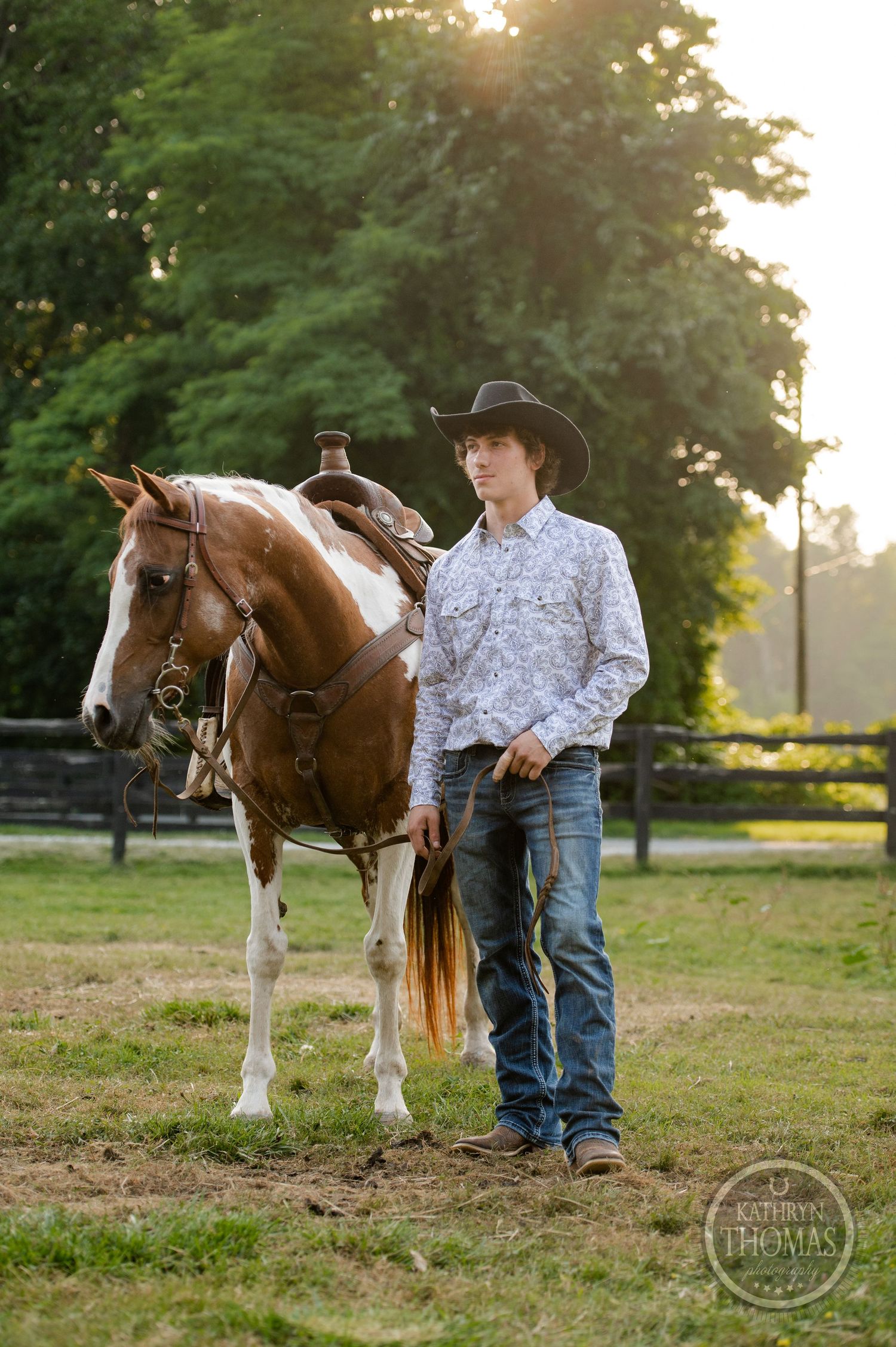 A brown and white horse stands with its handler in western attire against a wooded backdrop.