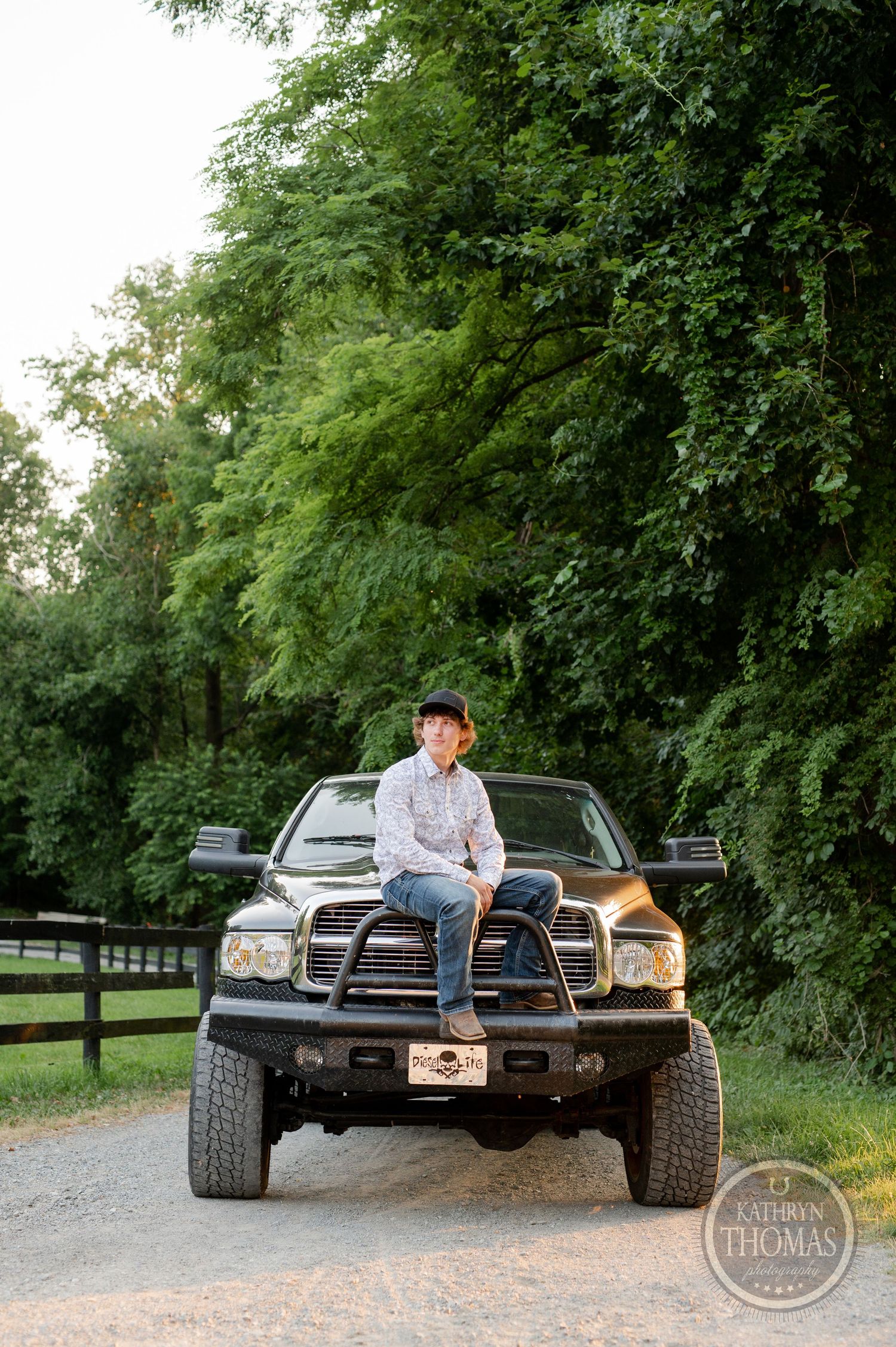 A person sits on the hood of a lifted black Dodge Ram truck on a rural road.