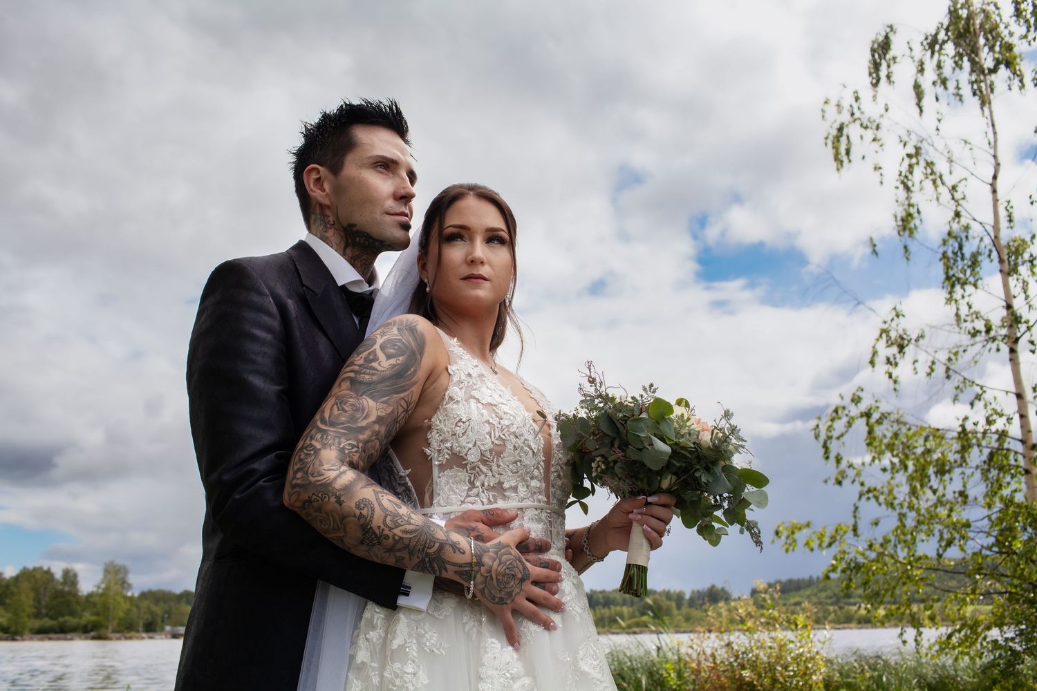 Newlyweds pose together in an outdoor setting with cloudy sky backdrop.