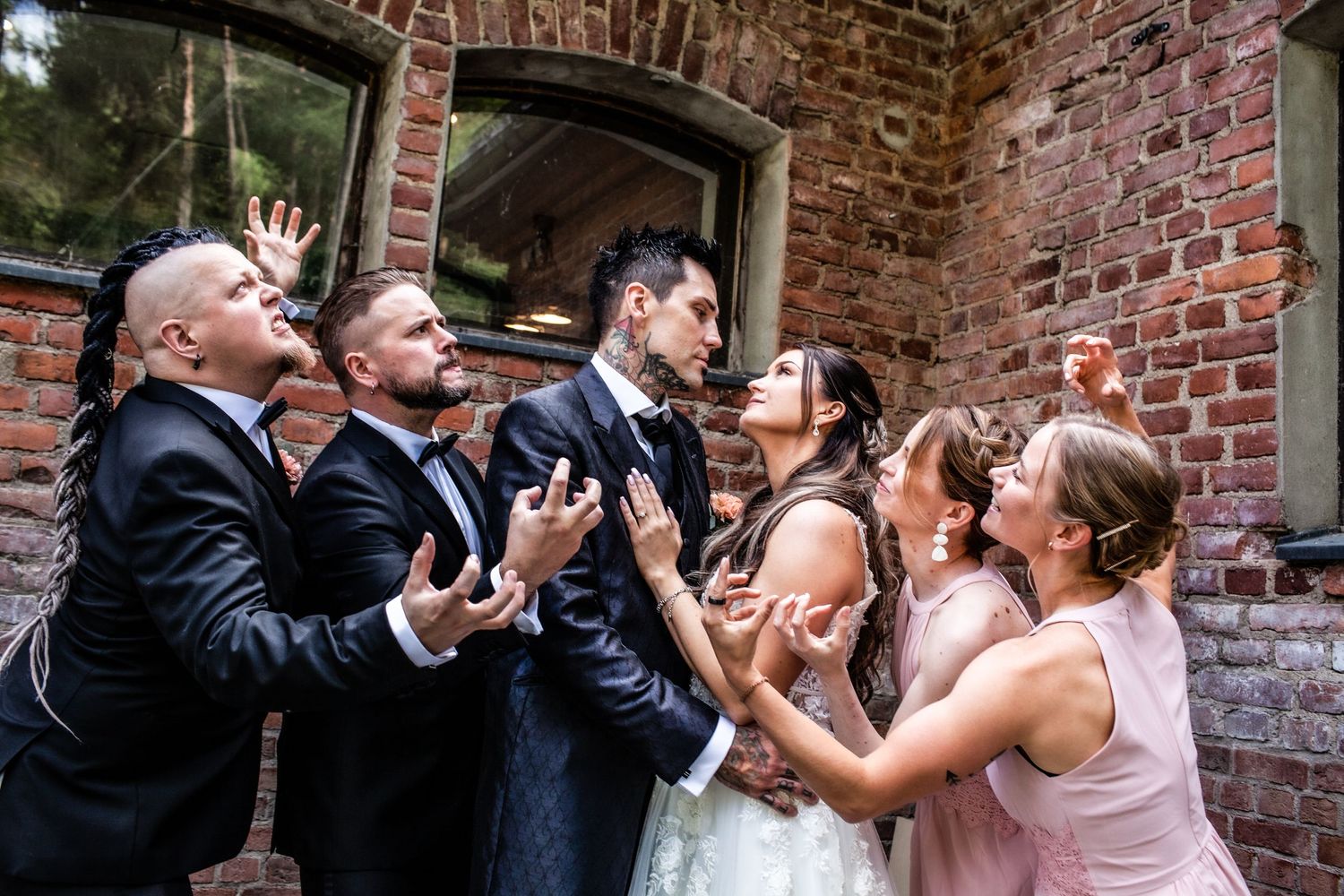 Wedding party celebrating and laughing together against a rustic brick background.