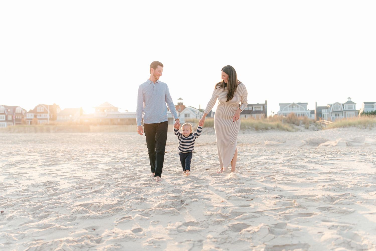 Parents and child holding hands, walking barefoot along the shoreline at spring lake beach during golden hour in autumn.