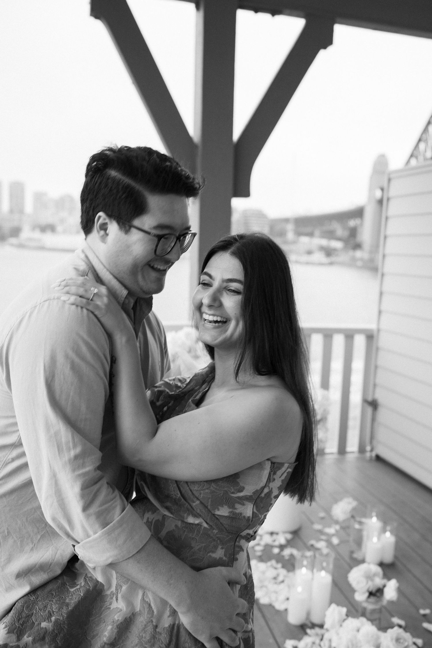 A black and white photo shows a couple laughing together on a decorated waterfront deck.
