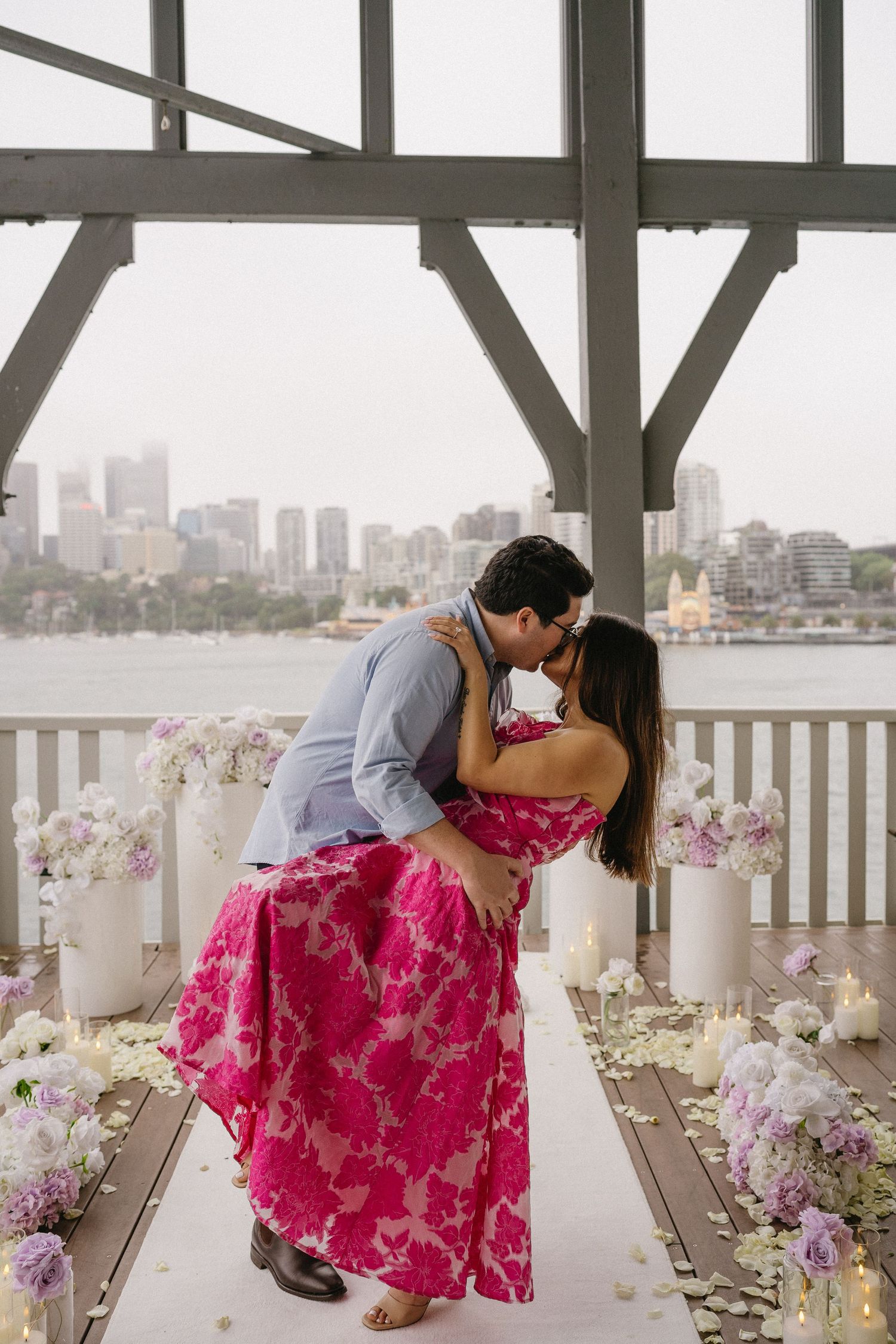 A romantic dip pose on a flower-decorated deck with city views and white candles.