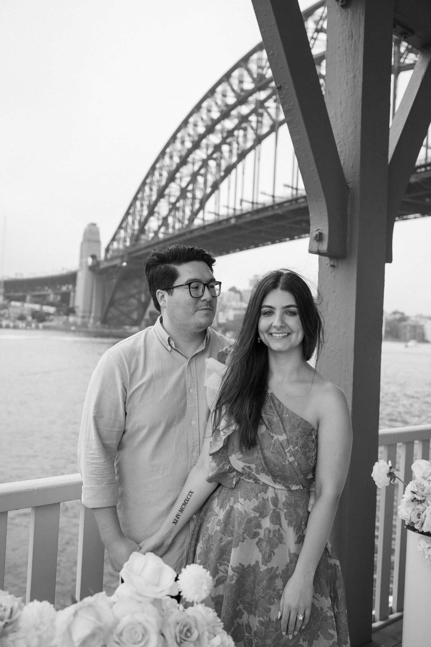 A black and white portrait of a couple with the Sydney Harbour Bridge visible behind them.