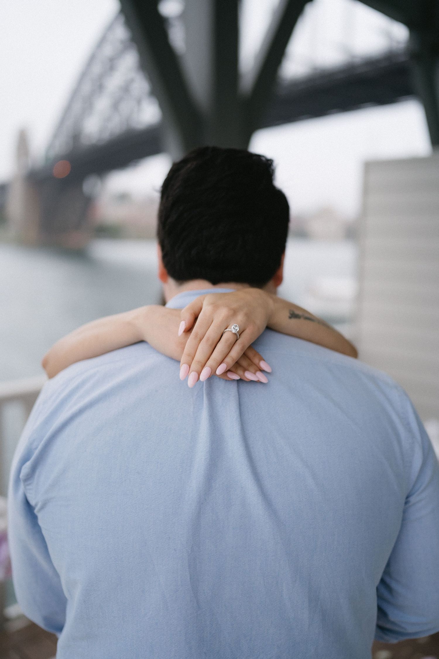 A close-up view of hands embracing with an engagement ring visible against a light blue shirt.