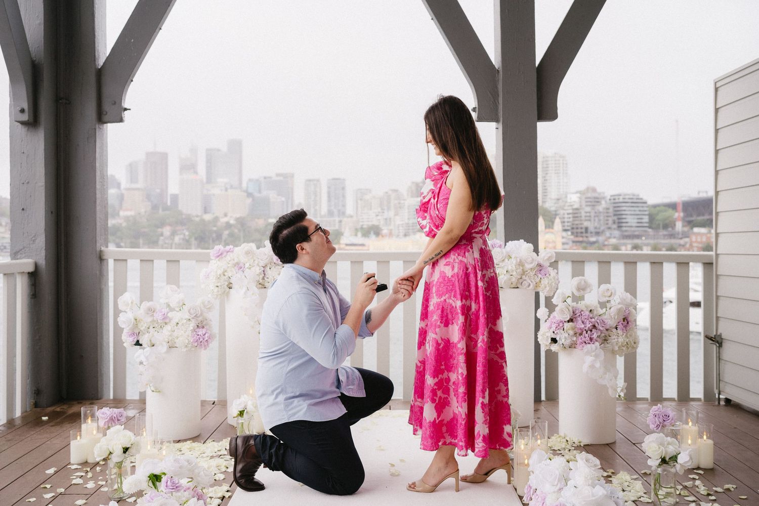 A proposal scene on a decorated balcony overlooking a city skyline.
