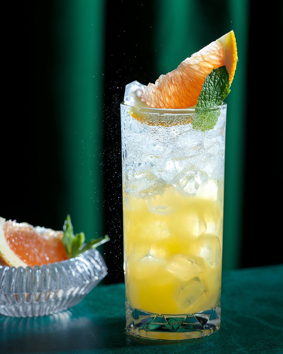 Refreshing grapefruit cocktail with ice, mint garnish, and citrus slice in a tall glass on a dark background.