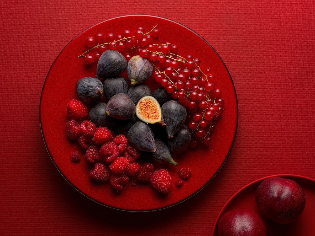 Red plate with fresh figs, raspberries, and red currants on a vibrant red background.