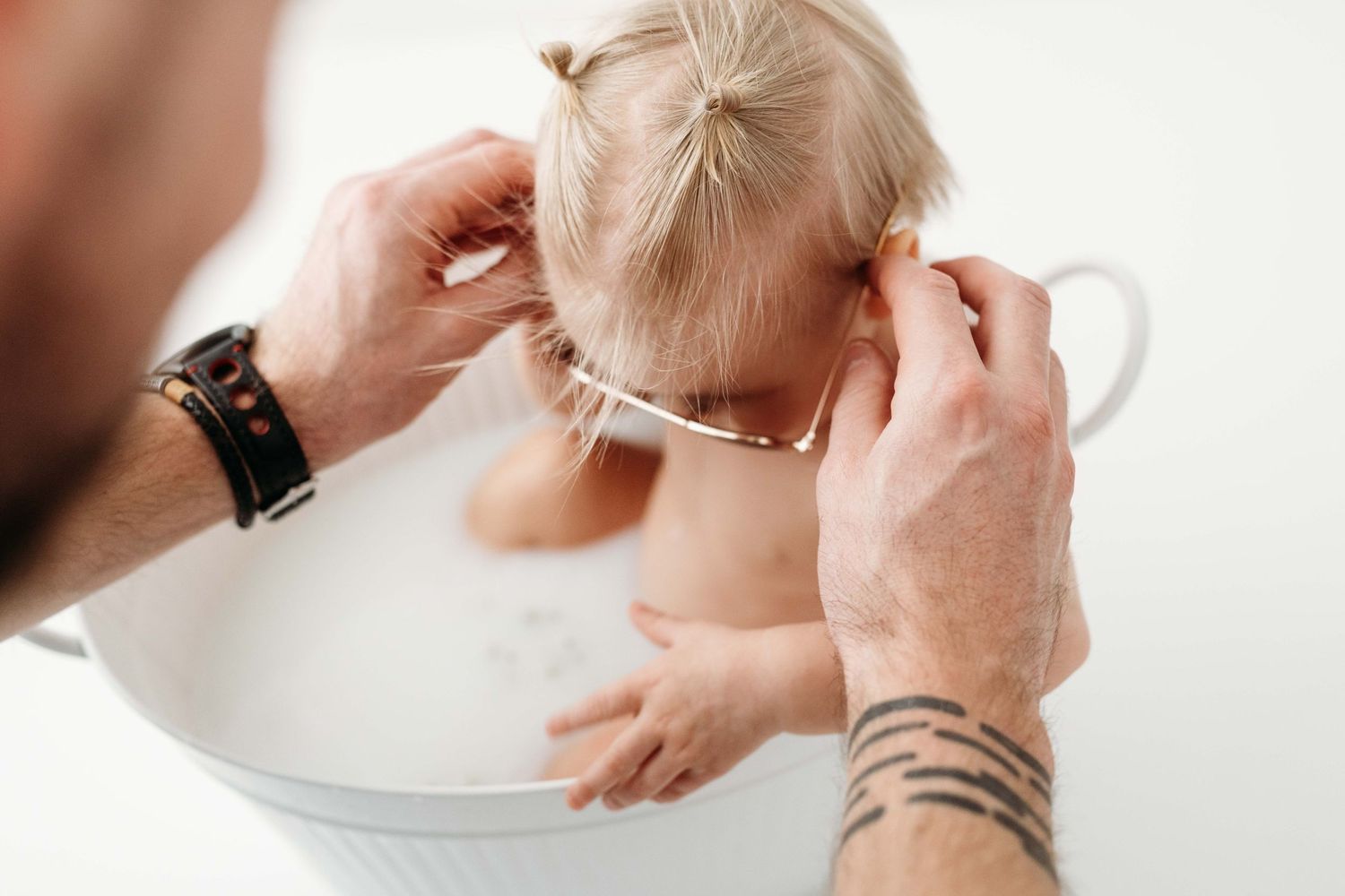 A person with tattooed arms styles blonde hair into a neat braid against a white background.
