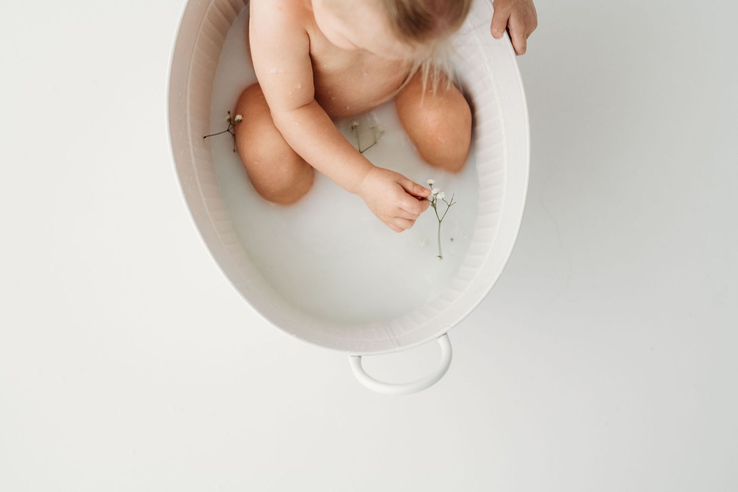 A baby's tiny feet soaking in a white ceramic basin filled with water on a light background.