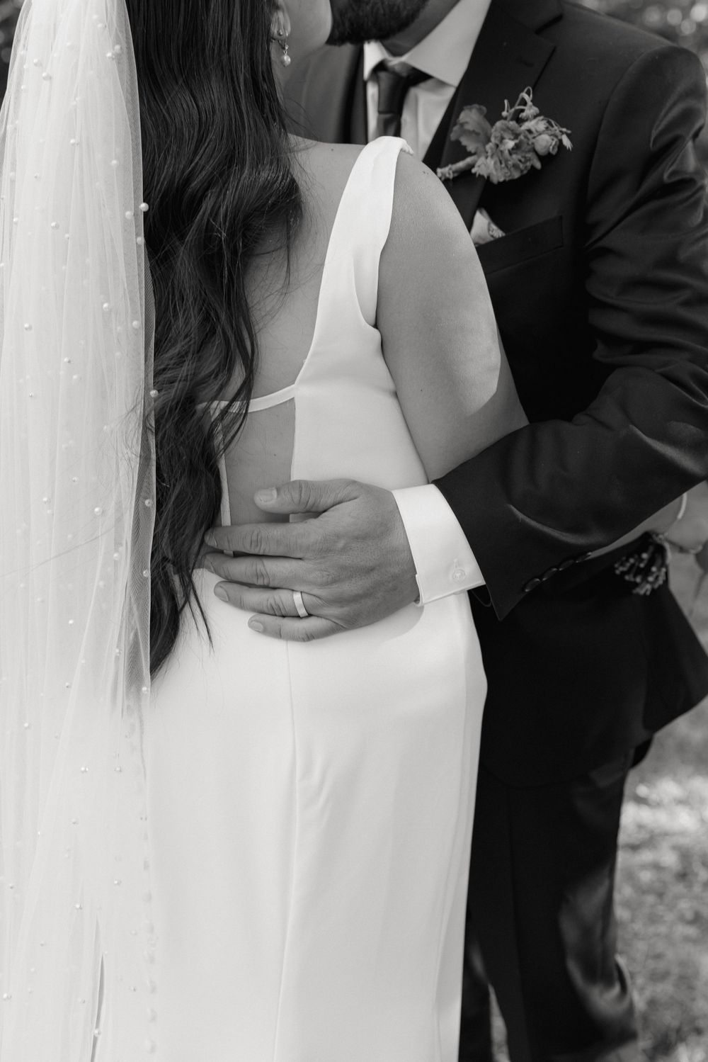 Black and white wedding photo showing couple embracing, with bride in sleek white dress and groom in dark suit.