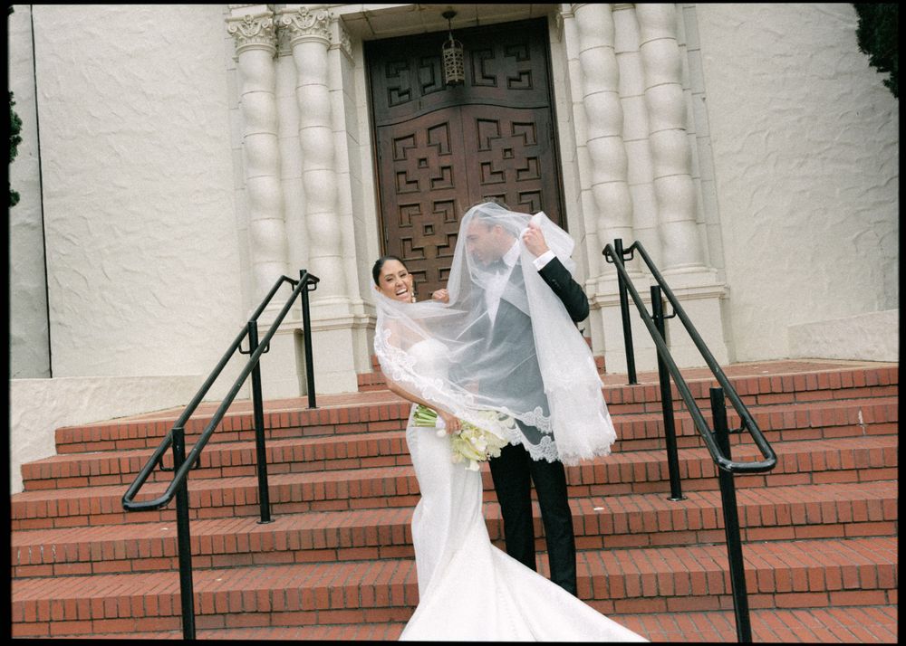 A romantic wedding moment captured on church steps as a couple shares a celebratory kiss in formal attire.