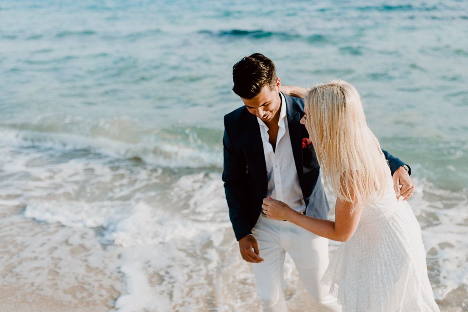 Couple in wedding attire sharing romantic moment on beach with ocean waves.