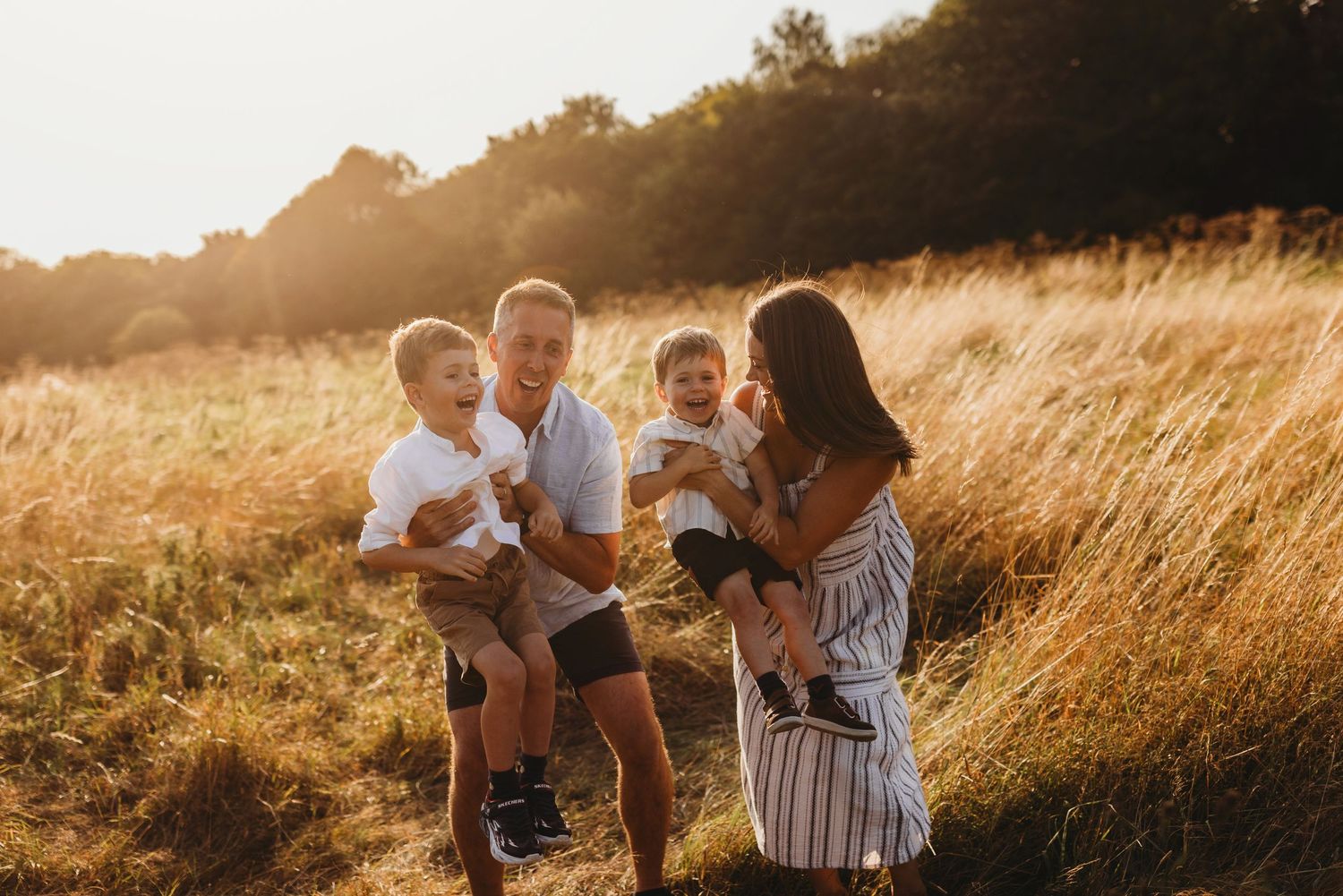 Family enjoying a golden sunset moment together in a tall grass field during summer.