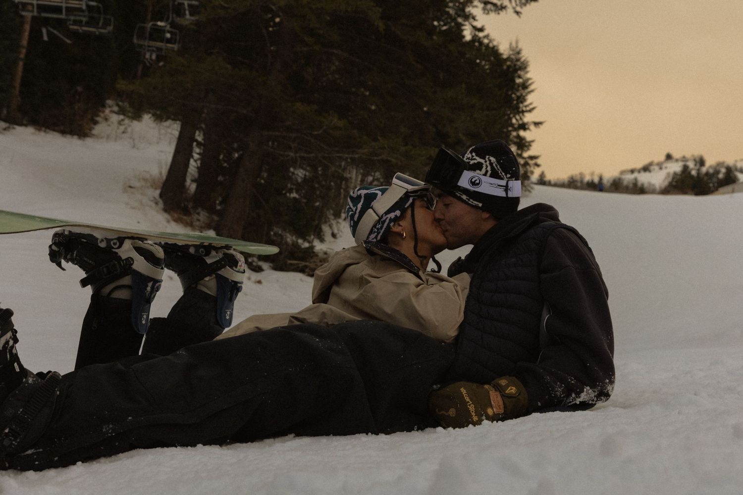 Winter sports enthusiasts preparing equipment on snowy mountain slope at dusk.