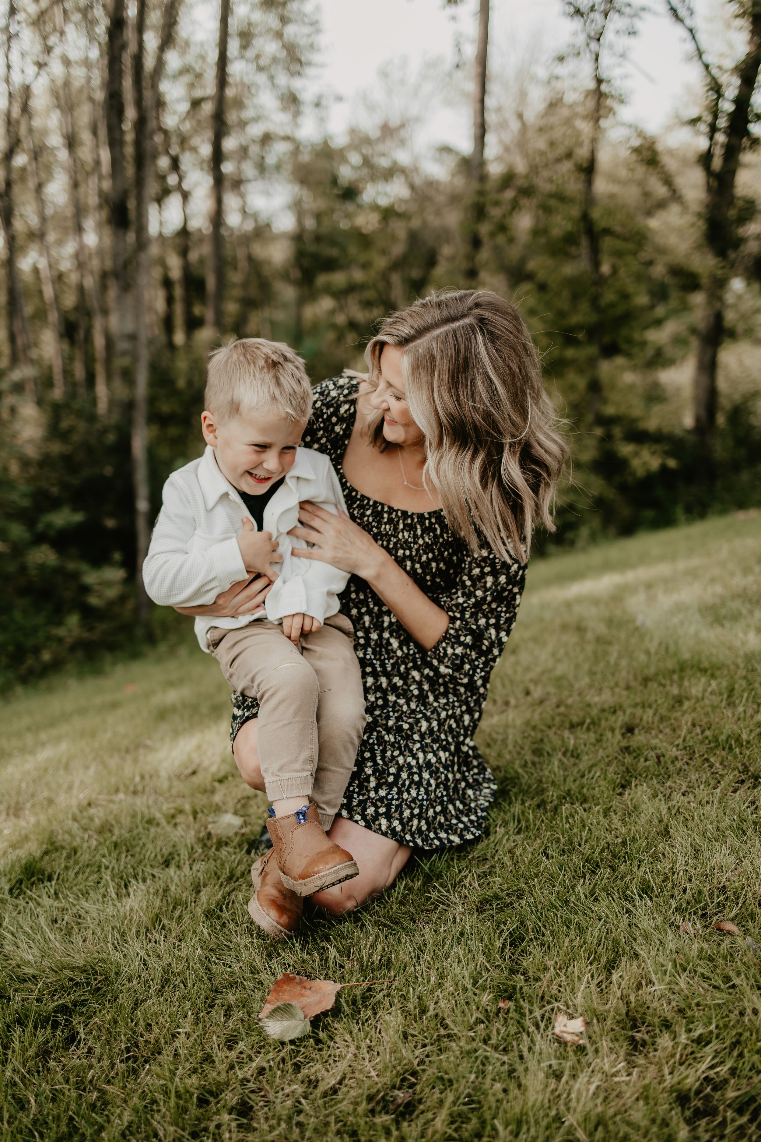A candid outdoor family moment captured on a grassy hillside with trees in the background during golden hour.