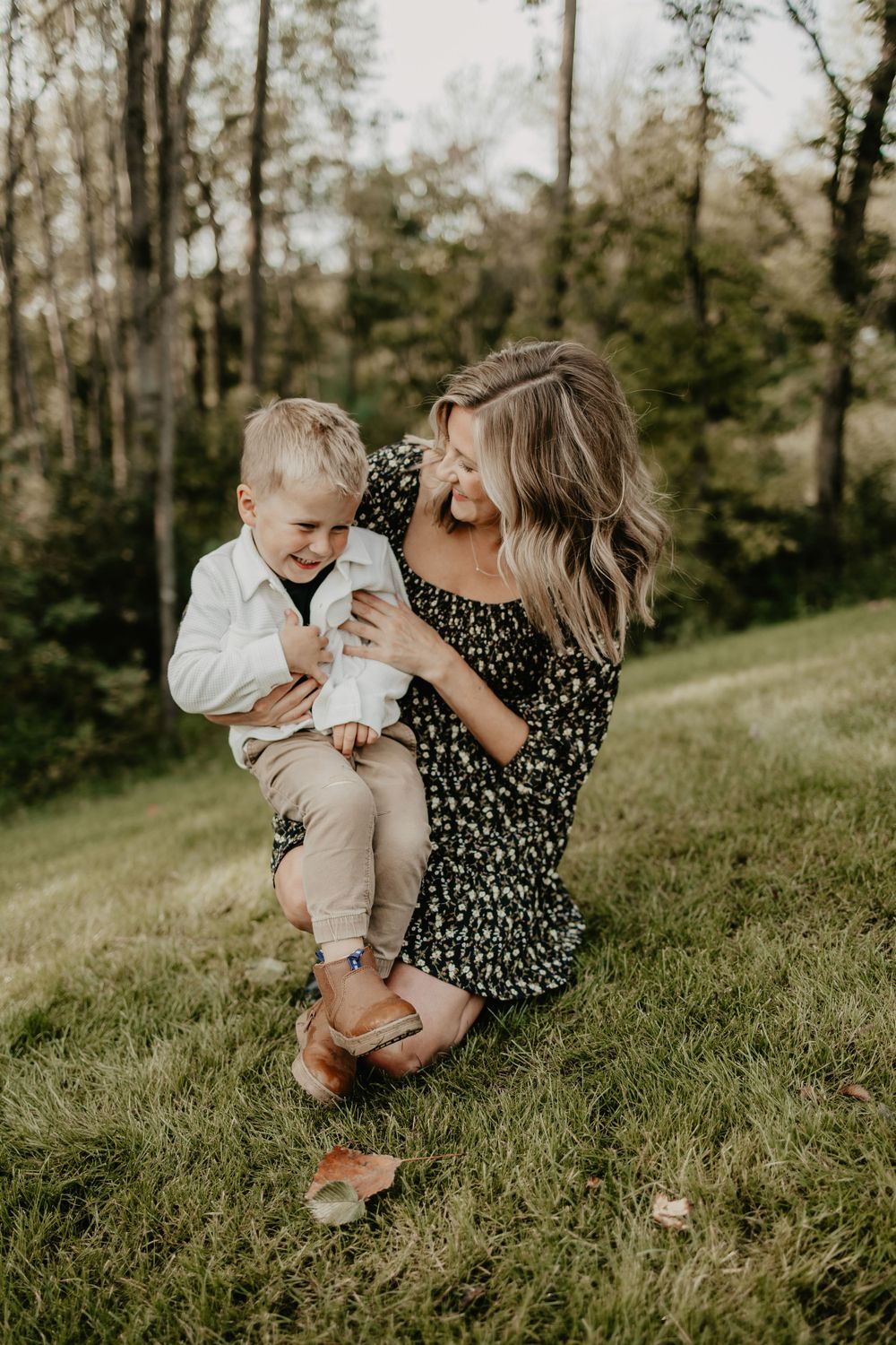 A candid outdoor family moment captured on a grassy hillside with trees in the background during golden hour.