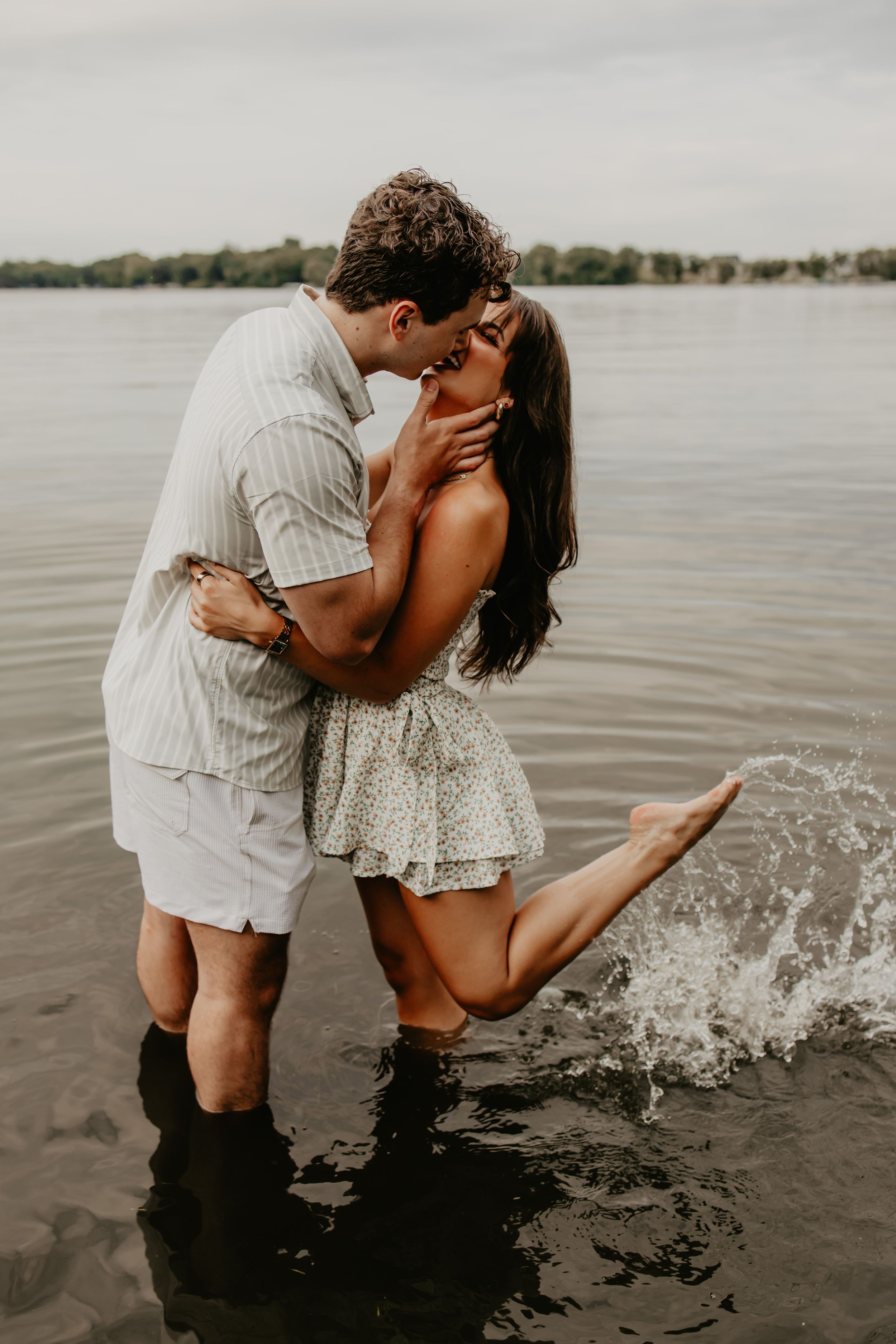 A romantic couple embraces while standing in shallow water during an engagement photoshoot by a lake.