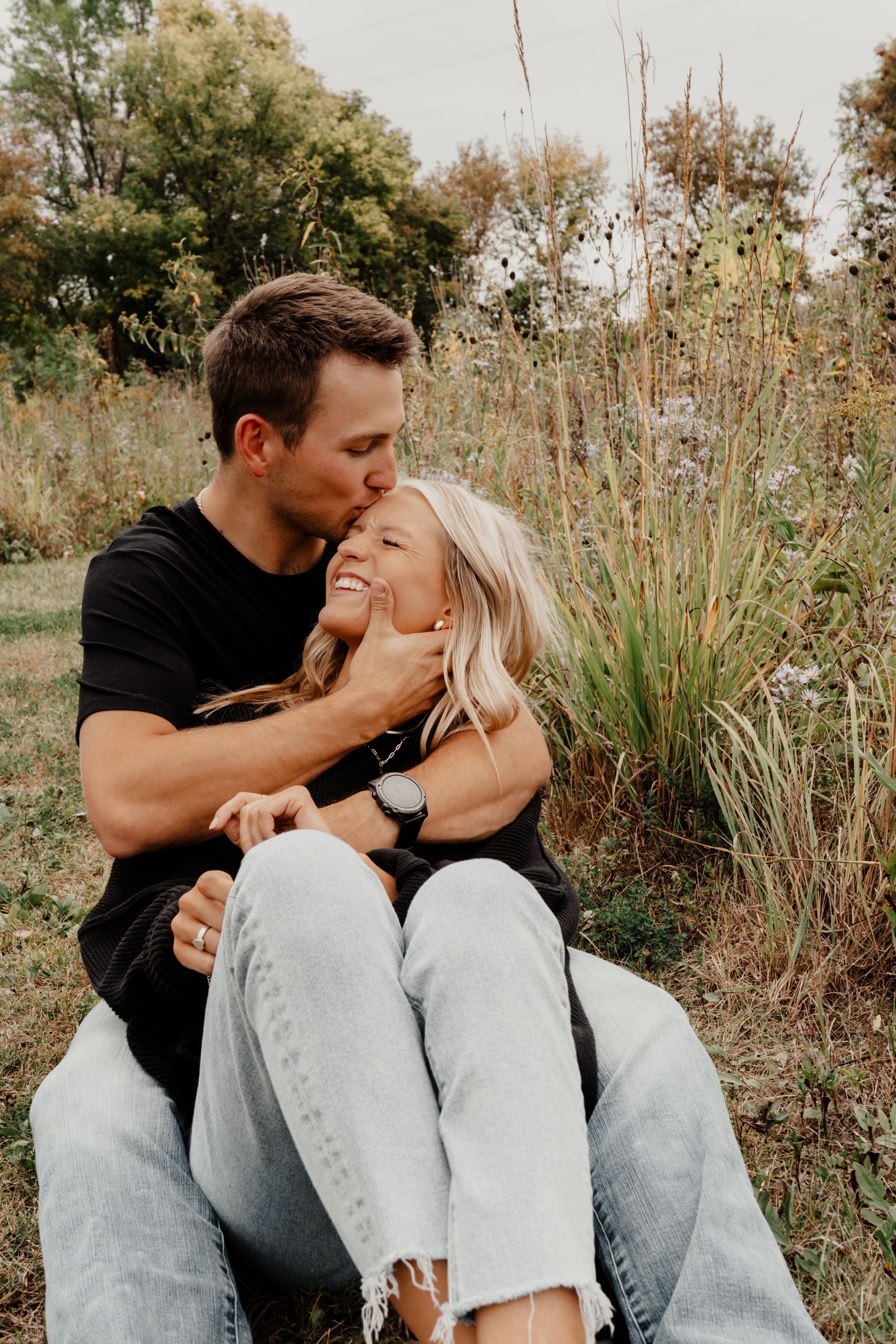 A romantic moment shared between a couple sitting in tall grass and autumn foliage.