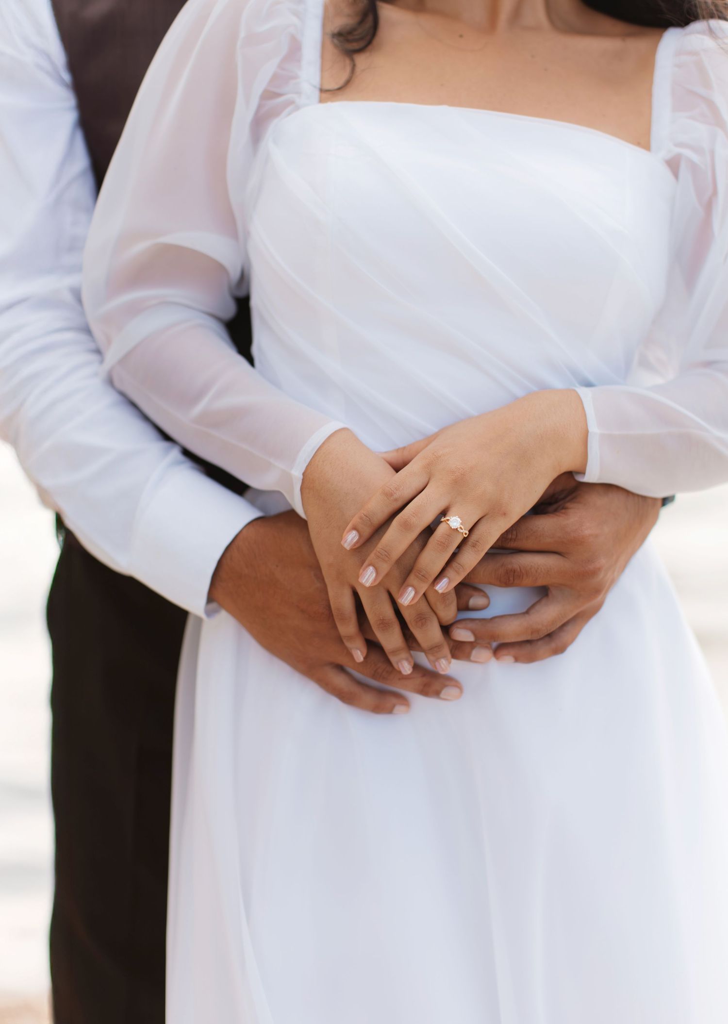Close-up of intertwined hands showing wedding rings against white dress and black suit.