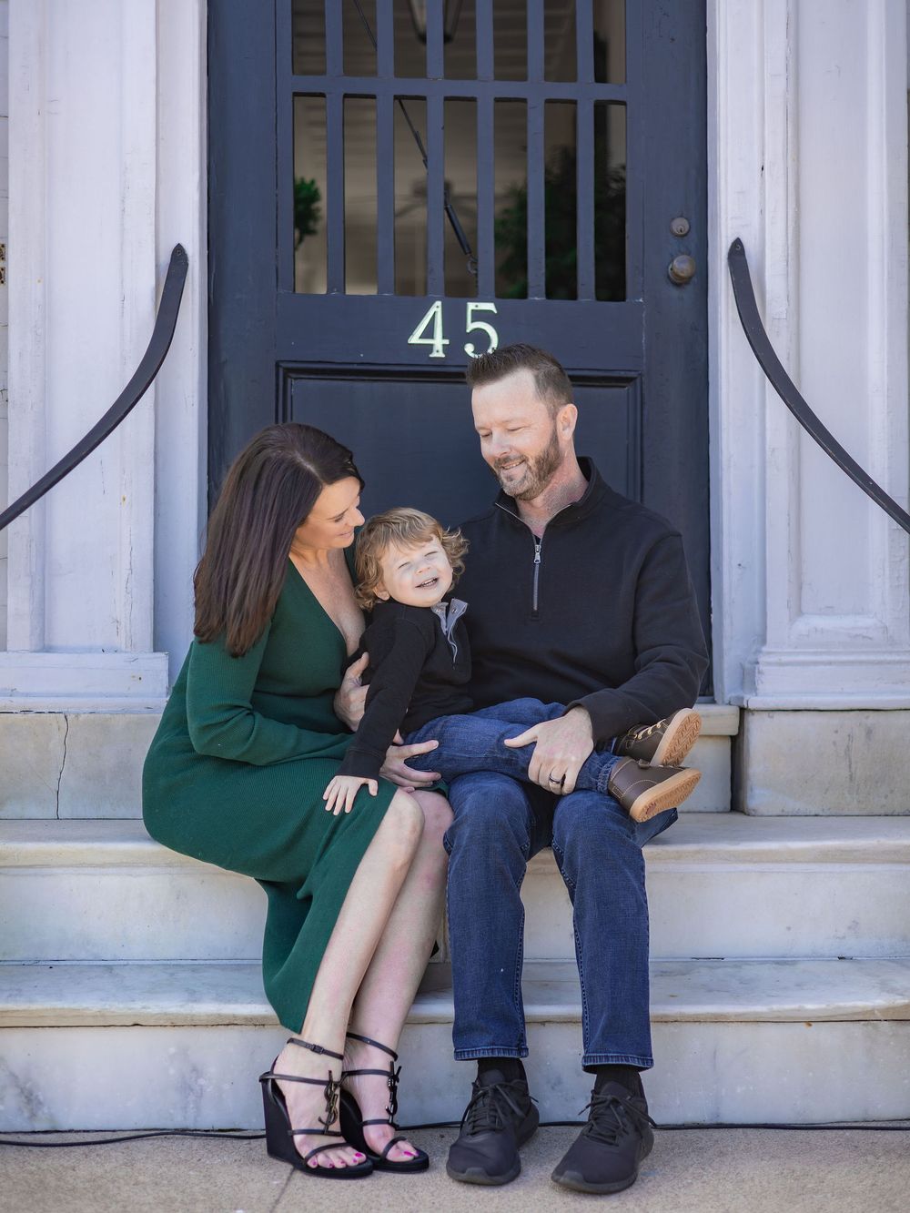 A couple sits together on white front porch steps sharing a tender moment in casual clothing.